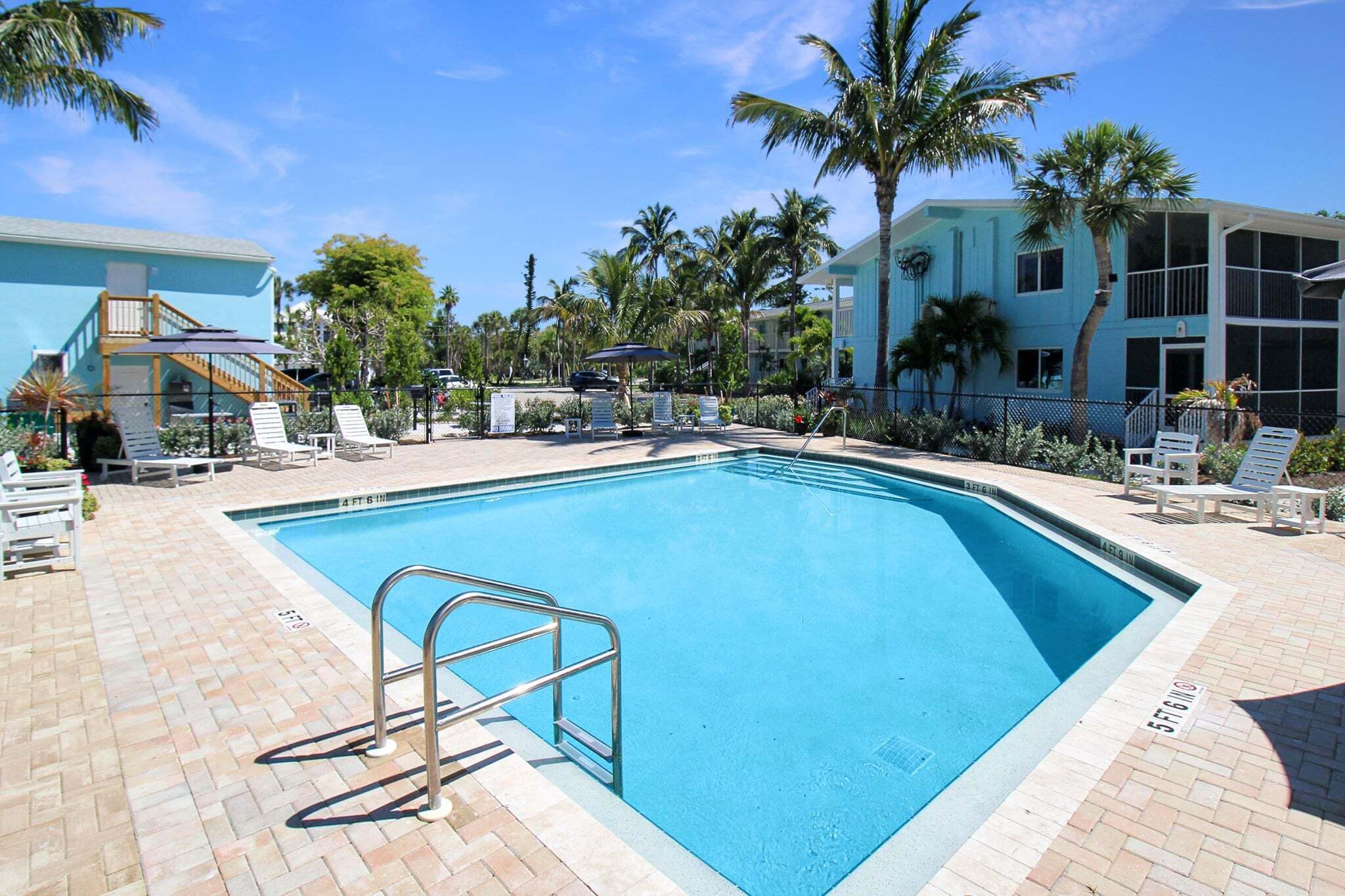 A swimming pool with lounge chairs, palm trees, and a building with a light blue facade.