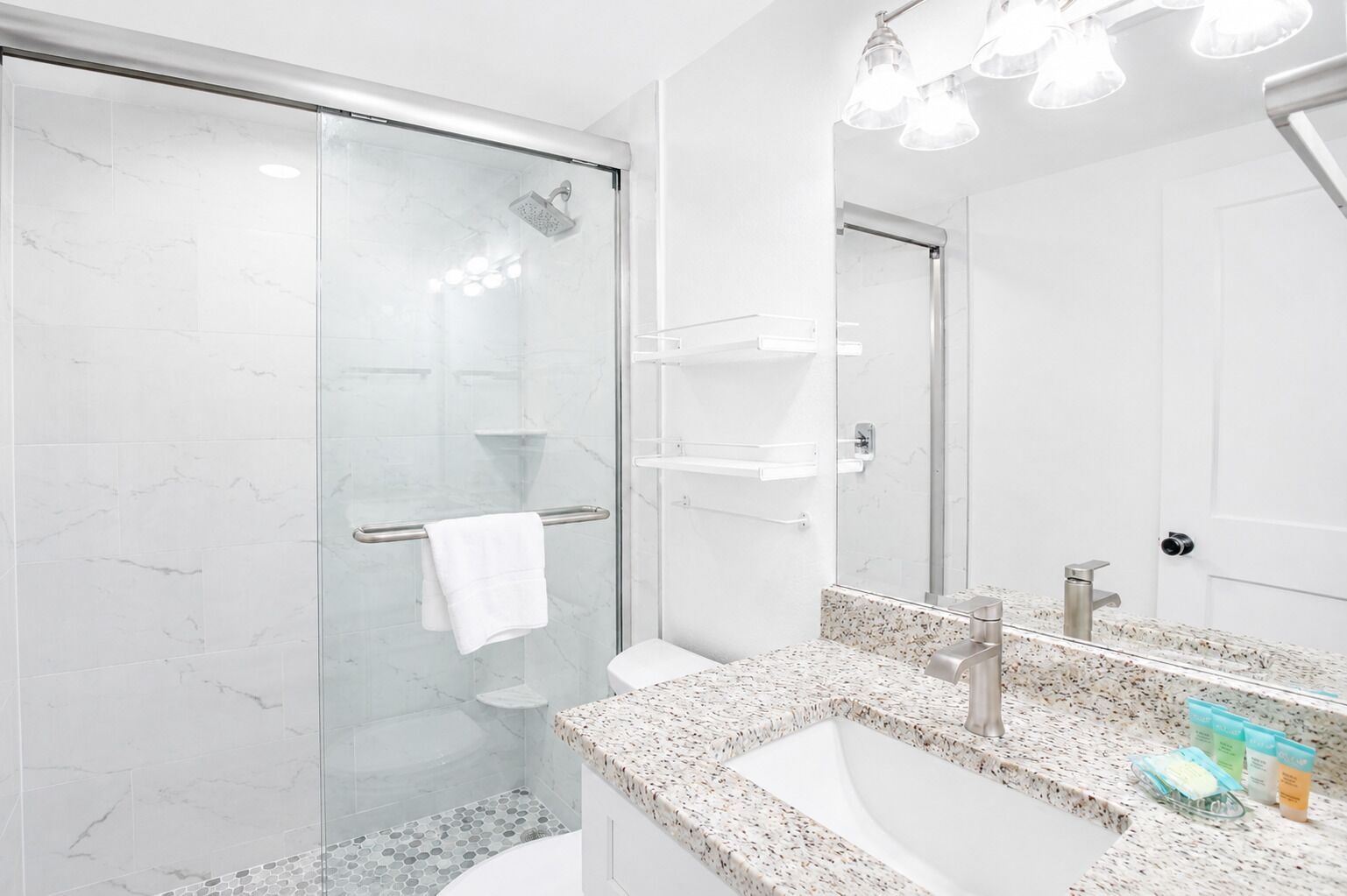 A modern bathroom with a glass shower enclosure, a granite countertop sink, and a large mirror.