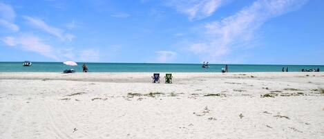 A beach with white sand, a few beach chairs, and a clear blue sky.