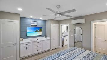 A bedroom with a bed, a ceiling fan, a TV, a bathroom with a mirror, and a door.