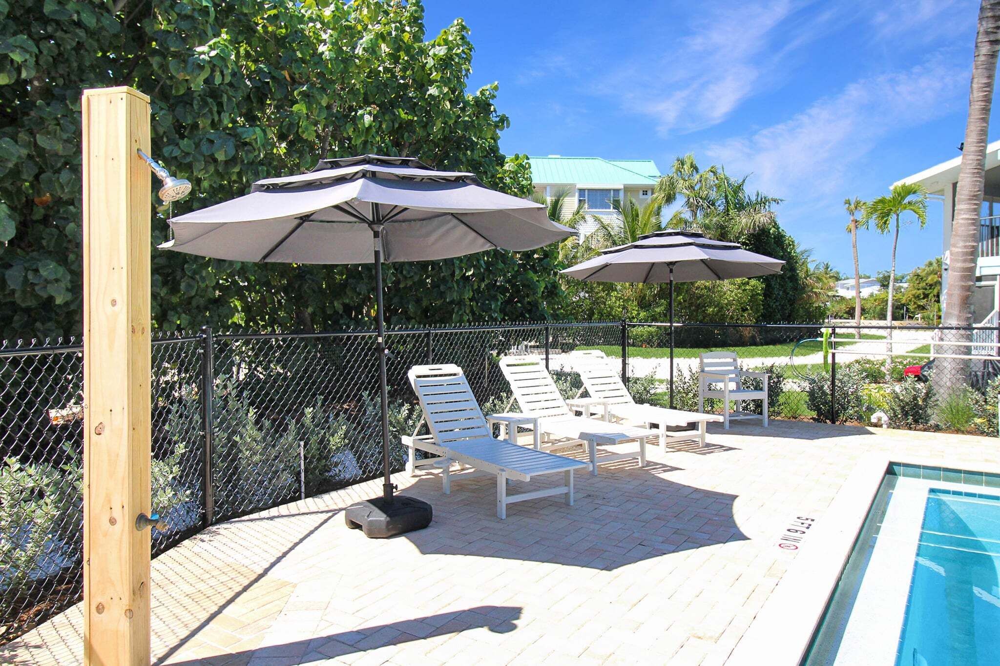 A poolside area with lounge chairs and umbrellas, a wooden post, and a chain-link fence.