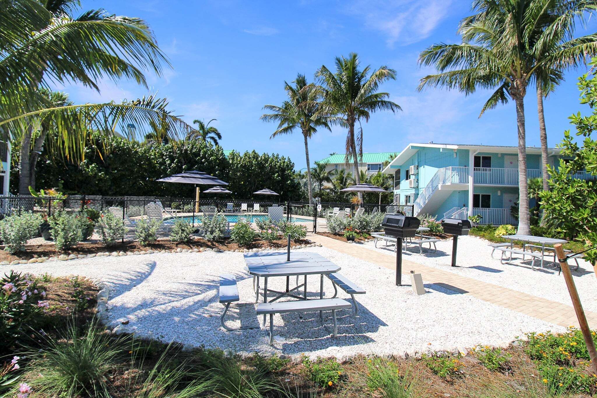 A pool area with lounge chairs, umbrellas, and a building with balconies.