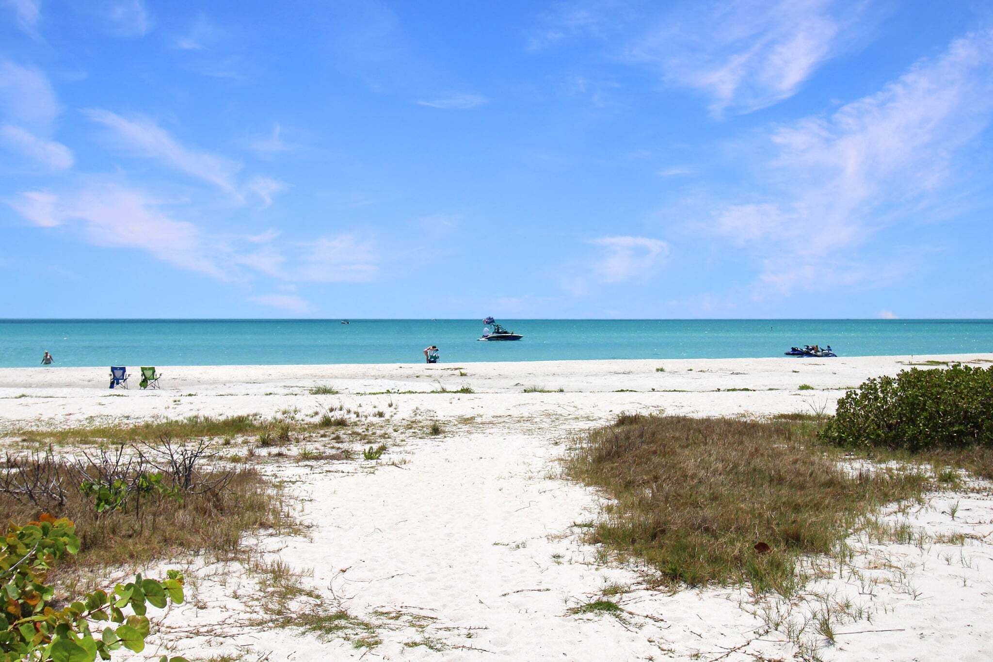 A beach with sand, sparse vegetation, and a clear blue sky.
