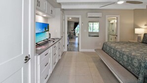 Una camera d'albergo con un letto, una televisione, una ventola a soffitto e un bagno parzialmente visibile attraverso una porta aperta.