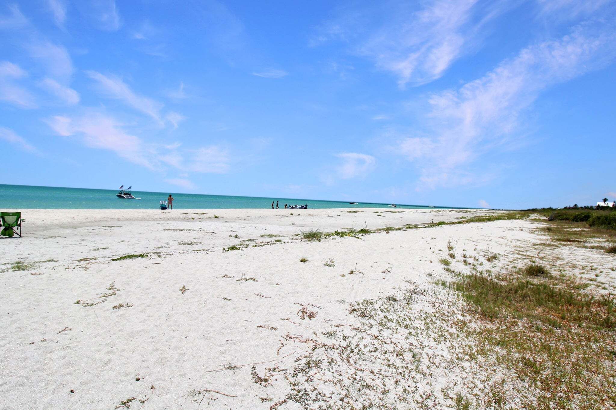 A beach with a clear sky, a boat, and a few people.