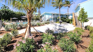Een resort met een zwembad, palmbomen en een terras met tafels en stoelen.