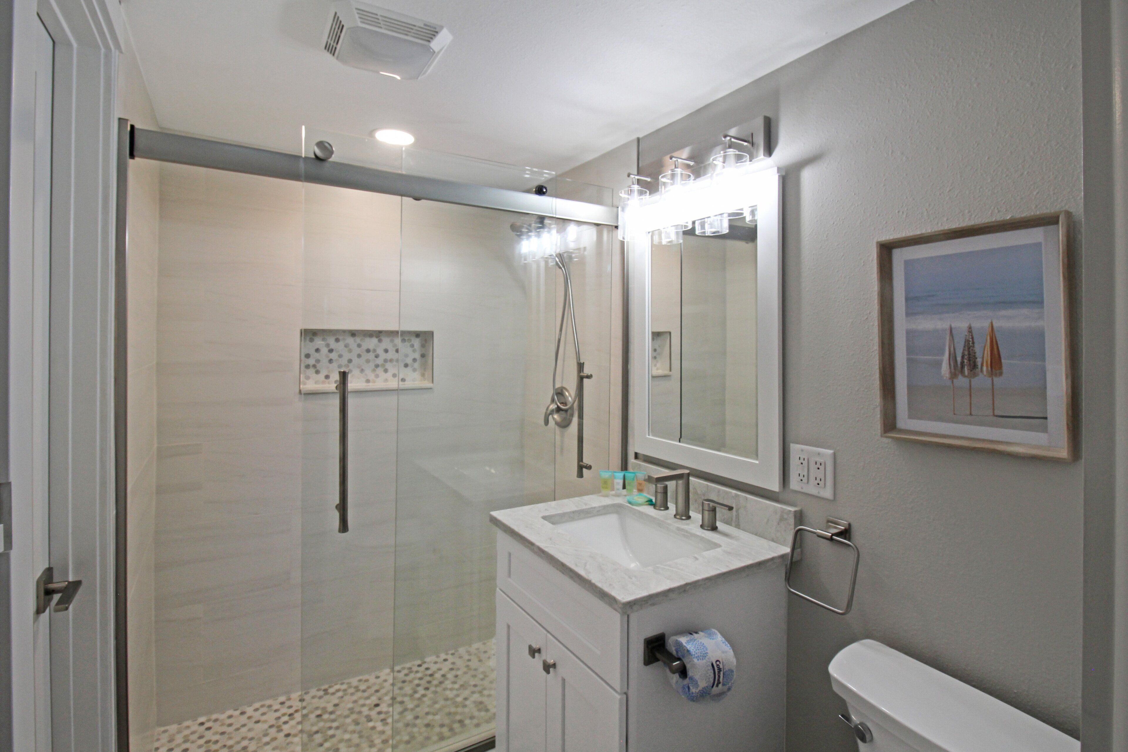 Un bagno con doccia vetrata, lavabo con specchio e water.