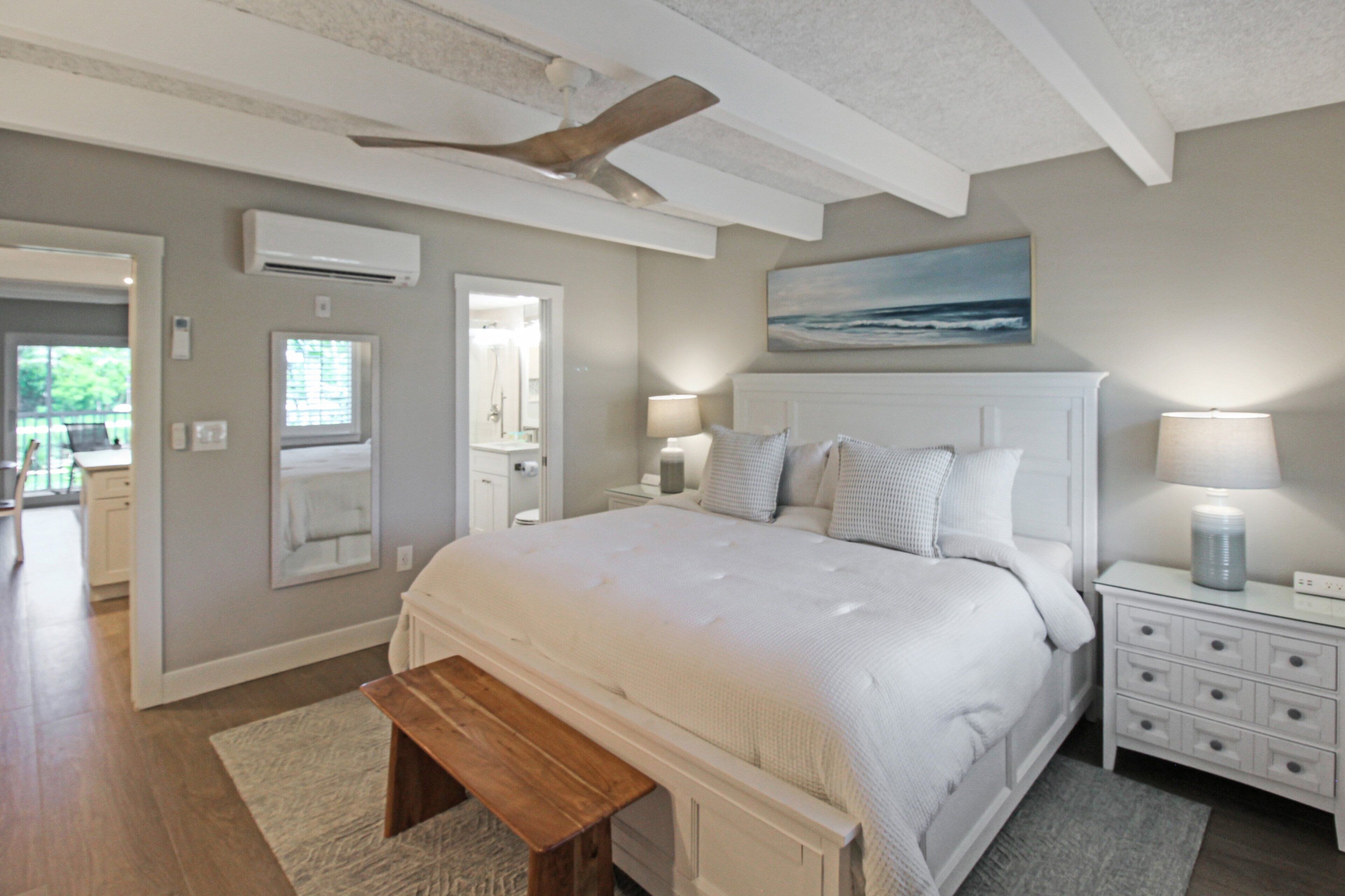 Une chambre à coucher avec un grand lit, des lampes de chevet, un ventilateur de plafond, un banc et un tableau accroché au mur.
