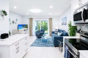 Eine moderne Küche mit integriertem Mikrowellenherd und Herd, ein Essbereich mit Tisch und Stühlen sowie ein Wohnzimmer mit Sofa und Fernseher.