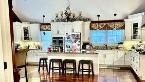 Una cocina amplia con una isla central, piso de madera y armarios blancos.