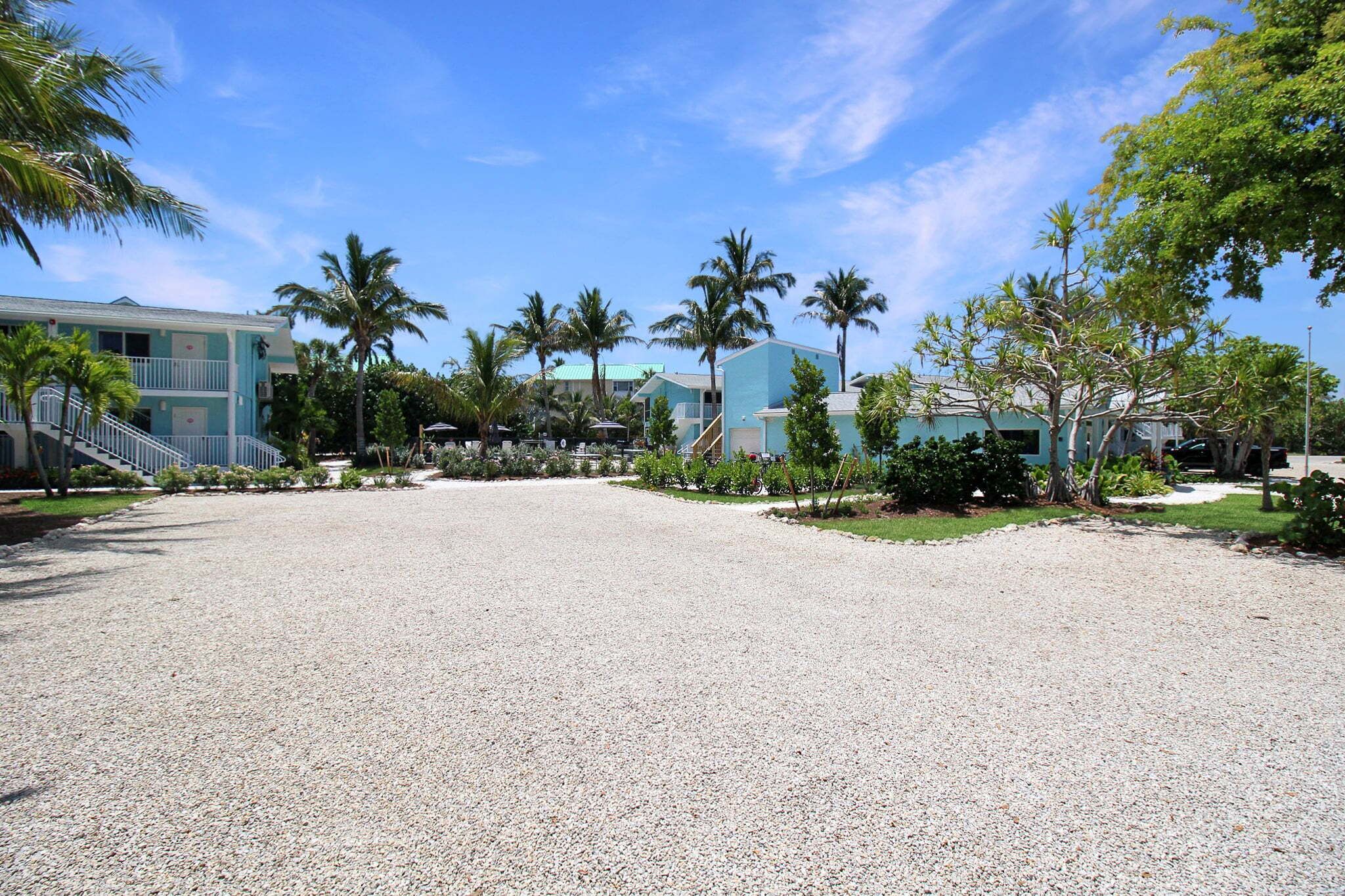 A hotel with a gravel driveway, palm trees, and a clear blue sky.