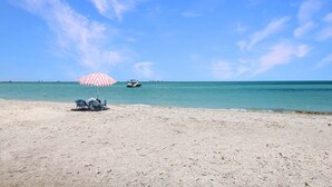 Una spiaggia con un ombrellone a righe, due sedie e una barca all'orizzonte.