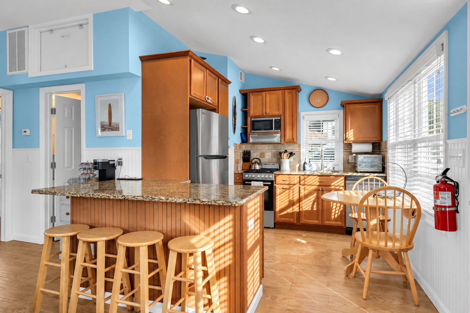 A kitchen with wooden cabinets, a stainless steel refrigerator, a microwave, and a stove. There are wooden stools and a dining table with chairs.