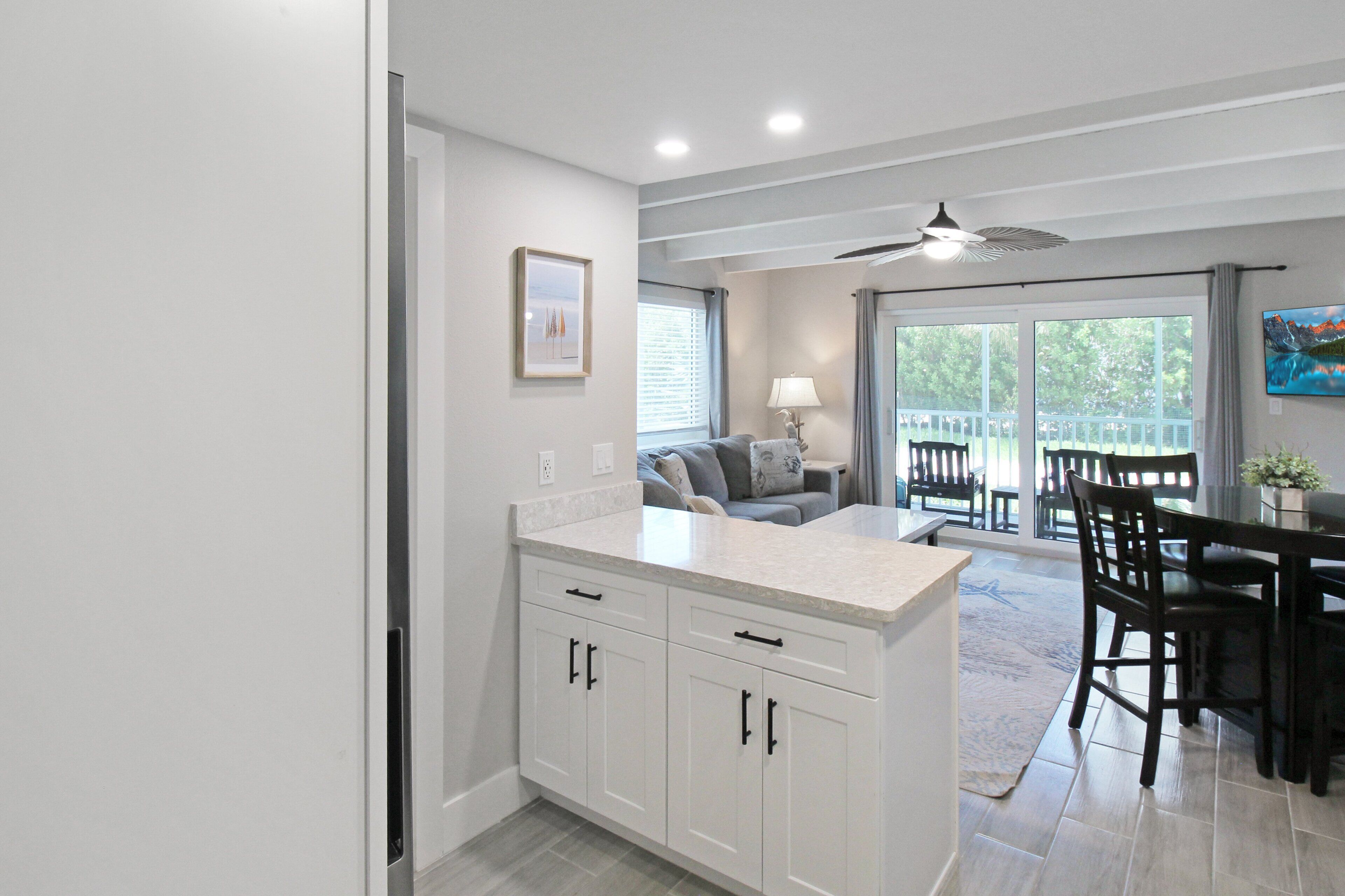 A modern kitchen with white cabinets, a dining area with a table and chairs, and a sliding glass door leading to a balcony.