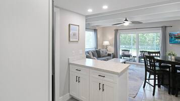 A modern kitchen with white cabinets, a dining area with a table and chairs, and a sliding glass door leading to a balcony.