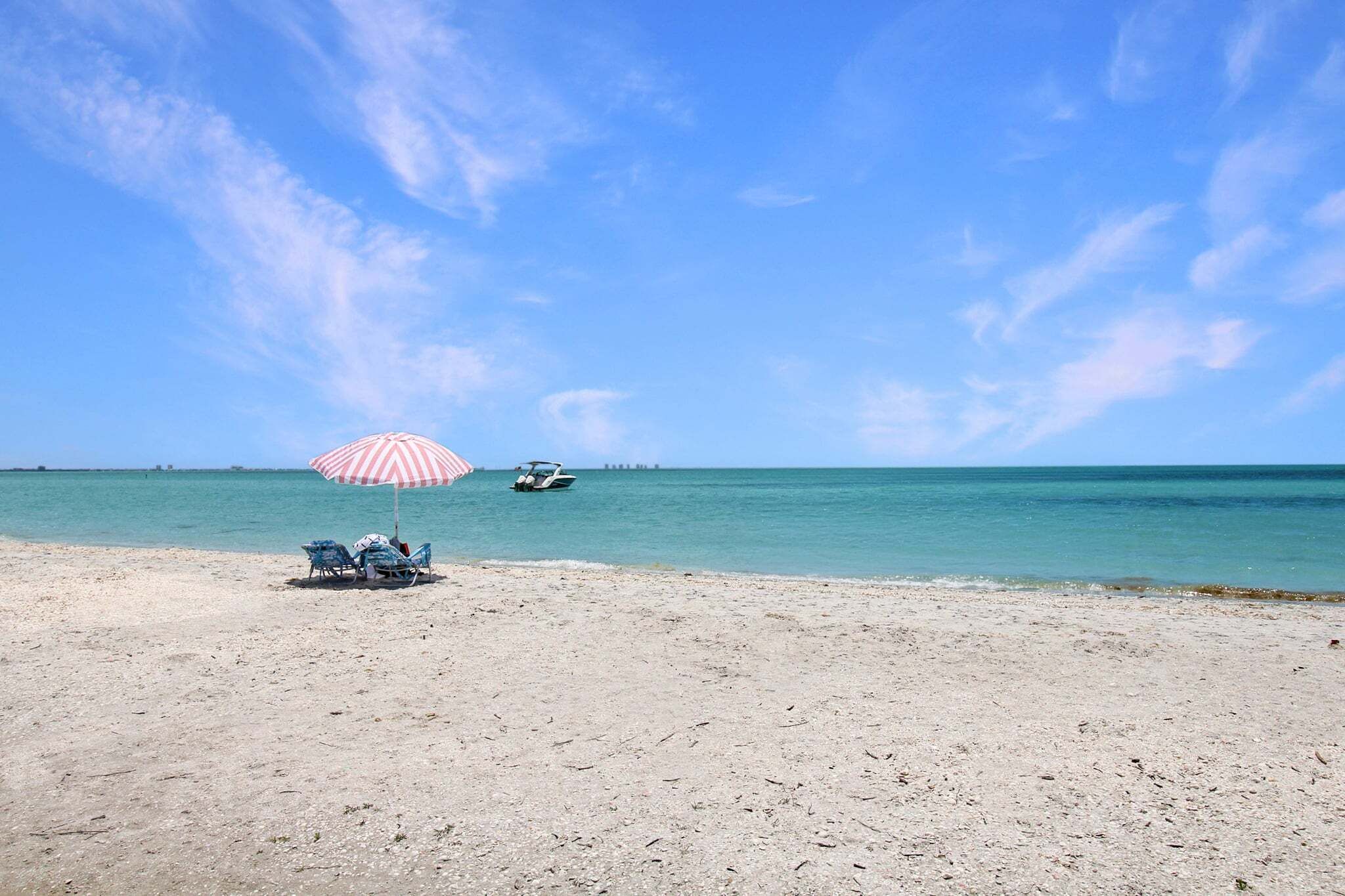 A beach with a striped umbrella, two chairs, and a boat in the distance.