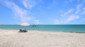 A beach with a striped umbrella, two chairs, and a boat in the distance.