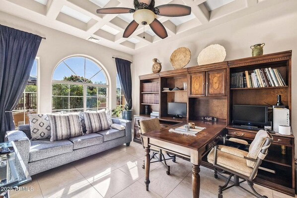 A spacious living room with a large window, a wooden dining table, a sofa, and a bookshelf.