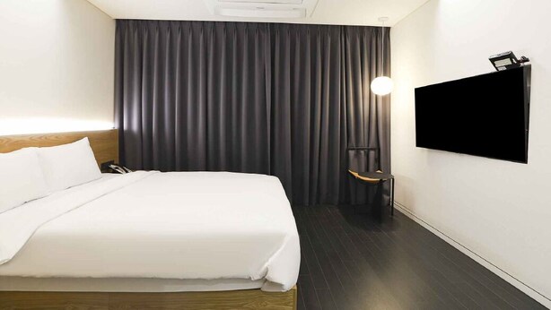 Une chambre d’hôtel avec un lit, un téléviseur à écran plat fixé au mur, des rideaux occultants et un climatiseur fixé au plafond.