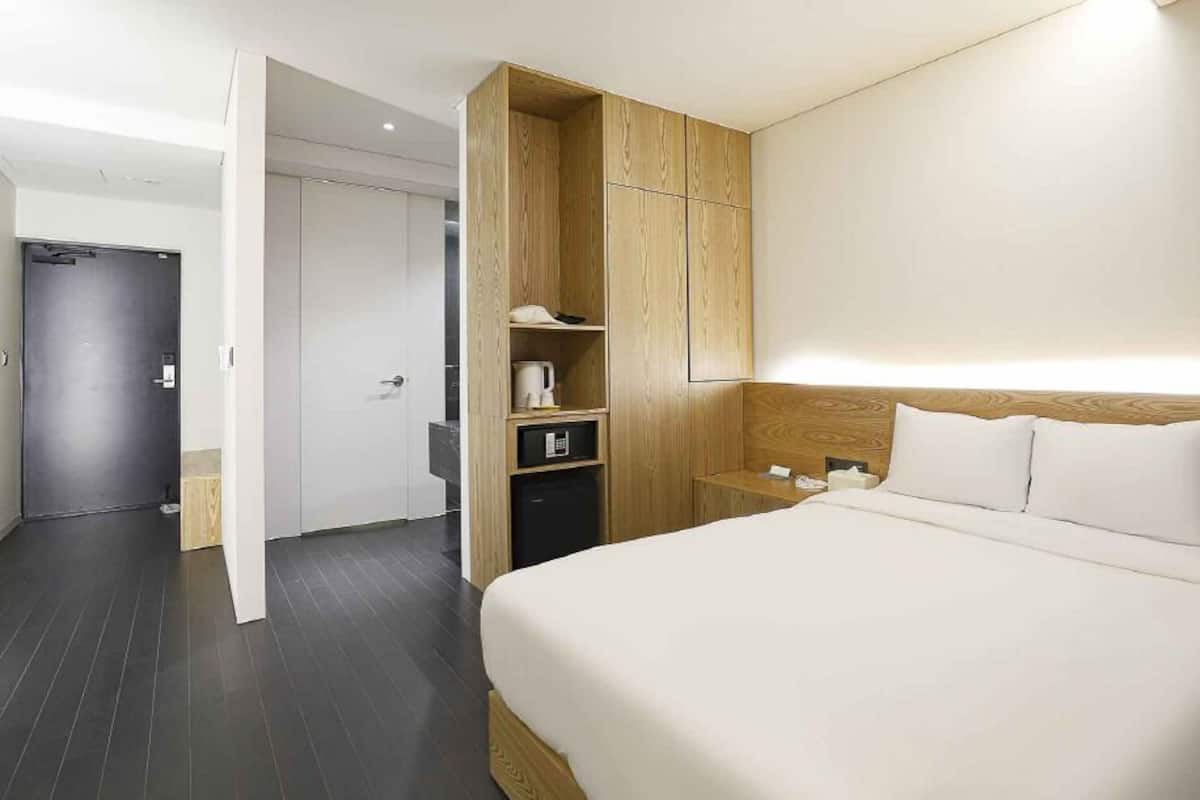 A modern hotel room with a large bed, wooden wardrobe, and a small bedside table.