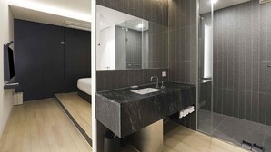 Une salle de bain moderne avec un lavabo en marbre foncé, un grand miroir et un espace douche.