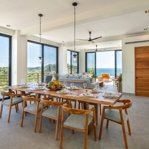 A spacious dining area with a high ceiling, large windows, and a view of the ocean.