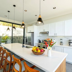 A modern kitchen with white cabinets, a large island, and a fruit bowl.