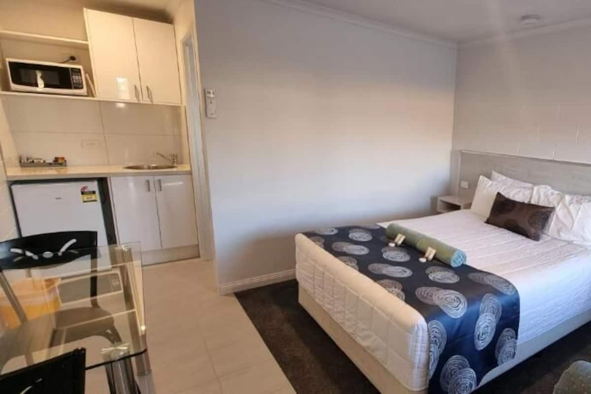 A compact room with a bed, a small kitchenette, and a seating area.