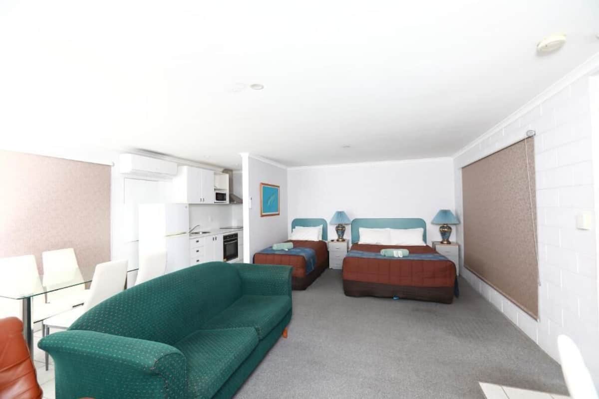 A hotel room with a green sofa, two beds, a kitchenette, and a dining area.