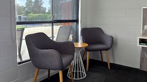 A room with two grey chairs, a small round table, and a large window with blinds. - Albatross Motor Inn (Lakes Entrance)