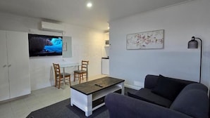 A living room with a sofa, a coffee table, and a TV mounted on the wall. There is a dining area with a table and chairs. - Albatross Motor Inn (Lakes Entrance)