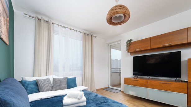 Ett modernt sovrum med en stor säng, en platt-TV, träskåp och utsikt över staden.
