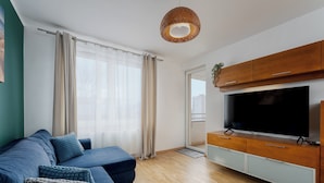 Ett modernt vardagsrum med en blå soffa, ett TV-bord i trä och ett stort fönster med gardiner.