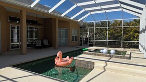 Una piscina con un galleggiante a forma di fenicottero rosa, circondata da un portico coperto con sedie e una struttura in vetro.