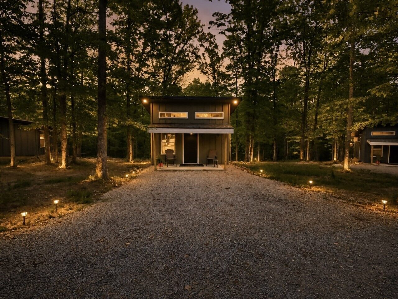 A two-story modern house with a gravel driveway, surrounded by trees.
