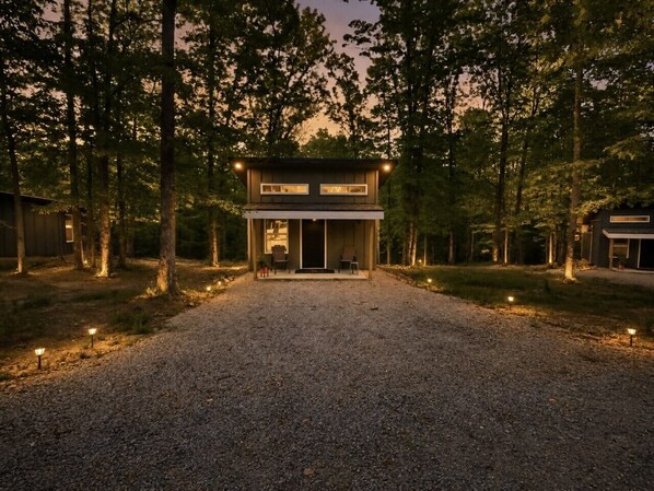A two-story modern house with a gravel driveway, surrounded by trees.