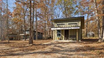 A two-story cabin with a front porch, surrounded by trees in autumn.