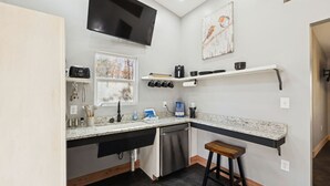 A compact kitchen with a built-in dishwasher, a TV mounted above the counter, and a small stool.