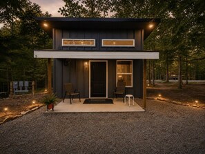 Ein modernes, zweistöckiges Gebäude mit dunkler Fassade, einer überdachten Veranda mit Sitzgelegenheiten und einem Schotterweg.