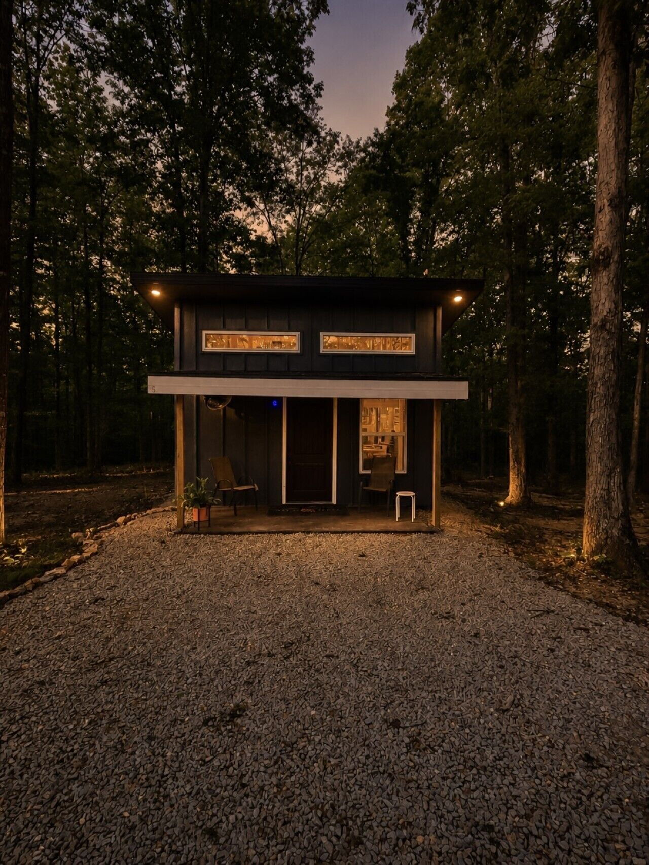 A modern, two-story building with a gravel driveway, surrounded by trees.