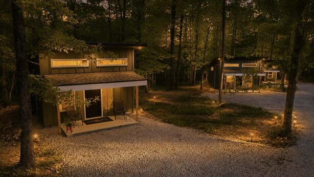 A modern house with a covered porch, surrounded by trees and gravel.