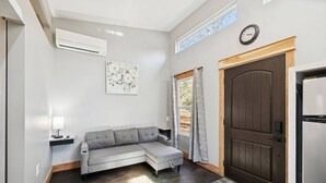 A modern interior with a grey sectional sofa, a wooden door, a white air conditioning unit, and a clock on the wall.