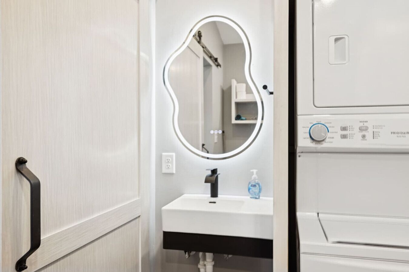 A bathroom with a vanity, a mirror, a hand dryer, and a washing machine.