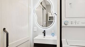 A bathroom with a vanity, a mirror, a hand dryer, and a washing machine.