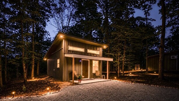 A modern house with a gravel driveway, surrounded by trees. - Cabins off the Trace: Cabin 4 (Summertown)