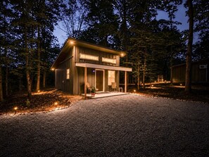 A modern house with a gravel driveway, surrounded by trees. - Cabins off the Trace: Cabin 4 (Summertown)