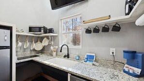 A kitchen with granite countertops, a stainless steel refrigerator, a microwave, a coffee maker, hanging pots, and a window with a view of trees. - Cabins off the Trace: Cabin 4 (Summertown)