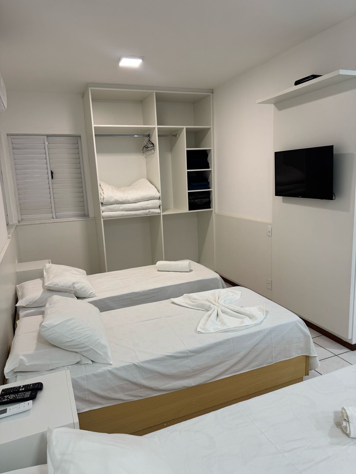 Quarto de hotel com duas camas, uma TV fixada na parede e um guarda-roupa com espaço para pendurar.