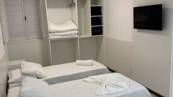 Quarto de hotel com duas camas, uma TV fixada na parede e um guarda-roupa com espaço para pendurar.