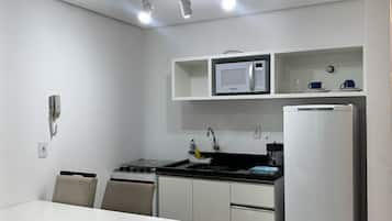 Cocina compacta con armarios blancos, un microondas, estufa y refrigerador. Hay una mesa de comedor con sillas y un pequeño estante sobre el microondas.